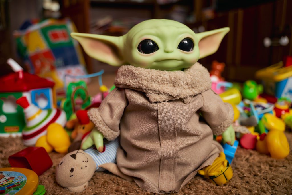 Black Friday | Baby Grogu, baby Yoda stands among the colorful toys. Realistic toy. Blurred background.