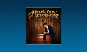 Brandon Flowers On Tour poster featuring a man in a suit posing on a red bench against wooden panel backdrop.